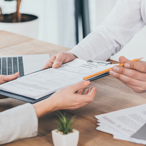 cropped view of businessman giving compensation claim form to woman at workplace