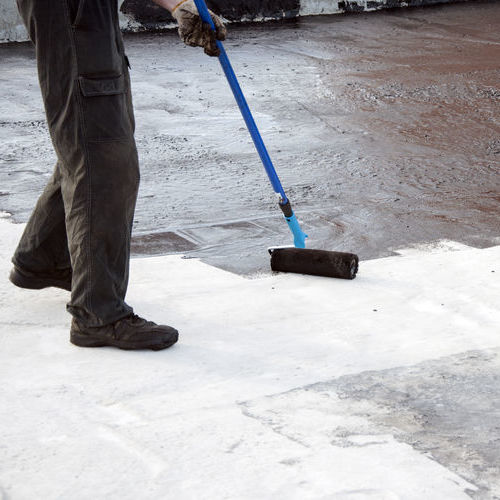 Roofer worker painting bitumen praimer at concrete surface by the roller brush, for waterproofing.